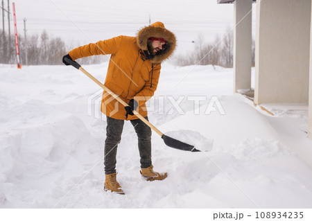Man is clearing the snow near house and on staircases hovelling at the winter season. Winter storm and season specific Man is clearing the snow near house and on staircases hovelling at the winter season. Winter storm and season specific 108934235