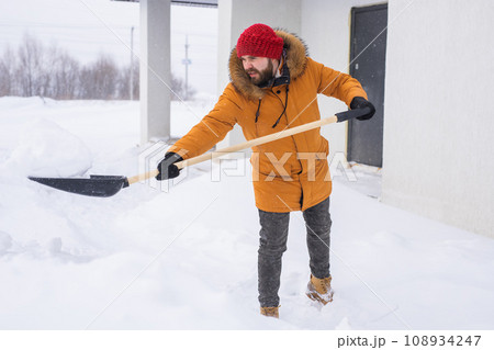 A man cleans and clears the snow in front of the house on frosty day. Cleaning the street from snow on a winter day. Snowfall and severe snowstorm in winter. A man cleans and clears the snow in front of the house on frosty day. Cleaning the street from snow on a winter day. Snowfall and severe snowstorm in winter. 108934247