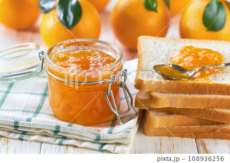 Homemade jam. A glass jar of orange jam on a white wooden table. Homemade orange marmalade and fresh oranges and green leaf on the kitchen table. 108936256