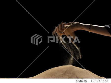 Hand releasing dropping sand on hill. Fine Sand flowing pouring through fingers hand against black background. Summer sand hill beach holiday vacation and time passing concept. Isolated freeze shot 108938228