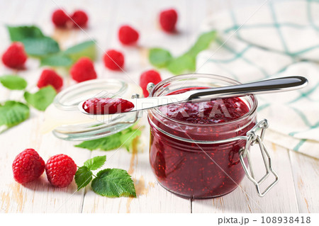 Sweet raspberry jam in jar with fresh berries on wooden table. Delicious raspberry jam on table close-up. Sweet raspberry jam in jar with fresh berries on wooden table. Delicious raspberry jam on table close-up. 108938418