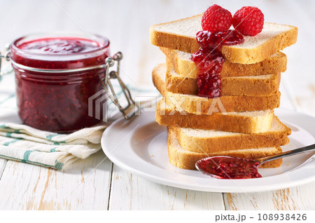 A stack of toast with raspberry jam on a dish close-up. Plate with pieces of toasted bread and tasty raspberry jam. 108938426