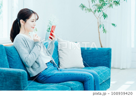 リビングでスマホを操作する女性。 108939420