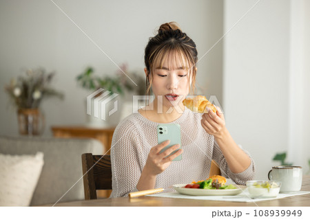 スマホを見ながら食事をする女性 108939949