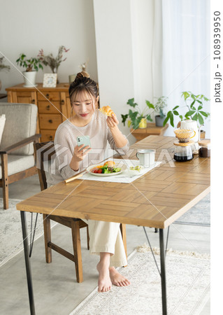 スマホを見ながら食事をする女性 108939950