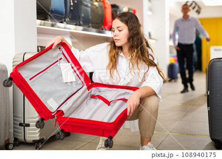 Focused girl checks the inside of an open travel suitcase Focused girl checks the inside of an open travel suitcase 108940175