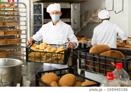 Baker in mask carrying crate with bread 108940186