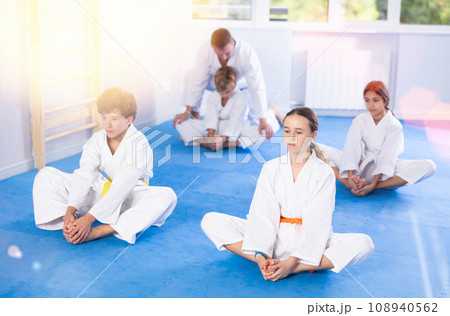 Children in white kimono sits in butterfly pose and practices stretching in sport gym 108940562