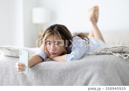 ビューティー ベッドに寝転びスマホを見る女性 ビューティー ベッドに寝転びスマホを見る女性 108940920