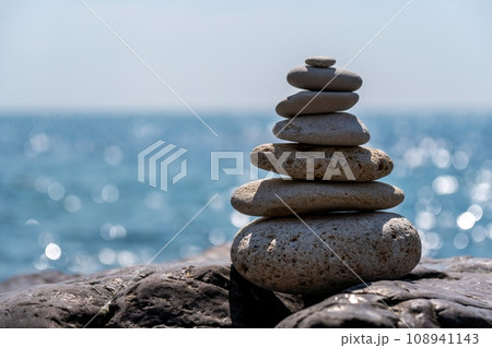 Pyramid stones on the seashore on a sunny day on the blue sea background. Happy holidays. Pebble beach, calm sea, travel destination. Concept of happy vacation on the sea, meditation, spa, calmness. 108941143