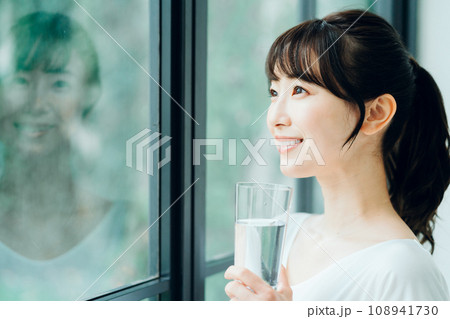 朝窓際で水を飲む女性。 108941730