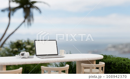 A white-screen laptop mockup, headphone, and a coffee cup on a table on a balcony with a nature view 108942370