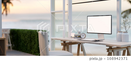 A cosy, minimalist home workspace with a white-screen computer mockup on a table against the window. A cosy, minimalist home workspace with a white-screen computer mockup on a table against the window. 108942371