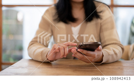 A woman using her smartphone while sitting at a table indoors. People and technology concepts 108942413
