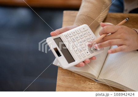 A woman using a calculator, checking her income and expenses and planning her household's financial. A woman using a calculator, checking her income and expenses and planning her household's financial. 108942424