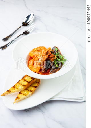 shrimp and mussels with herbs in a white plate with toasted bread, side view 108945448