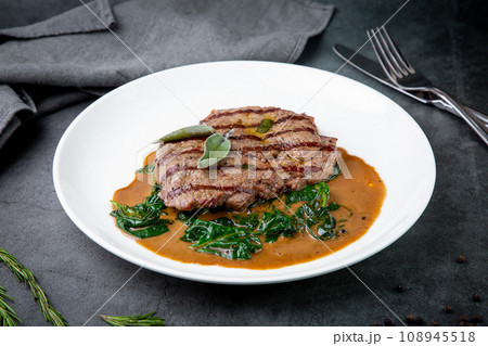 steak in gravy with herbs on it on a white plate 108945518