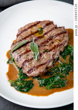 steak in gravy with herbs on it on a white plate 108945526