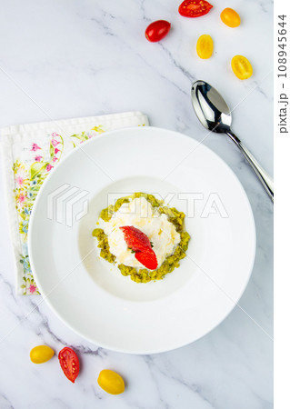 curd dessert with strawberries on top in a white plate on a marble background, side view 108945644