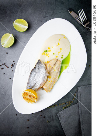 pieces of fried fish with sauce and fried lemon on a white plate top view pieces of fried fish with sauce and fried lemon on a white plate top view 108945690