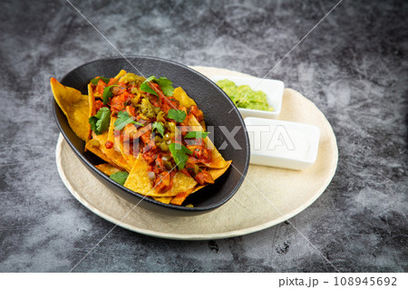 nachos with sauce, meat and herbs in a black plate, side view nachos with sauce, meat and herbs in a black plate, side view 108945692