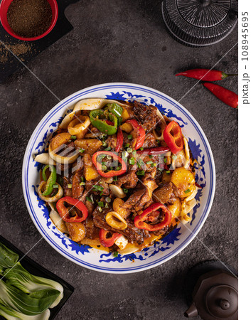 noodles with bell pepper, potatoes, meat and herbs in a plate with a pattern top view 108945695