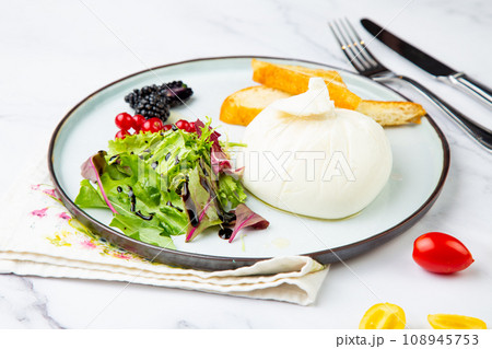mozzarella with spinach, cherry tomatoes, wild berries and bread in a round plate side veiw 108945753