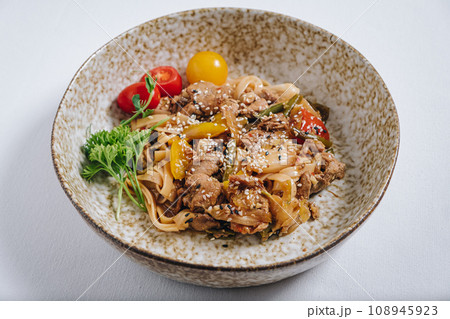 udon noodles with duck meat, herbs, sesame seeds and cherry tomatoes side view 108945923