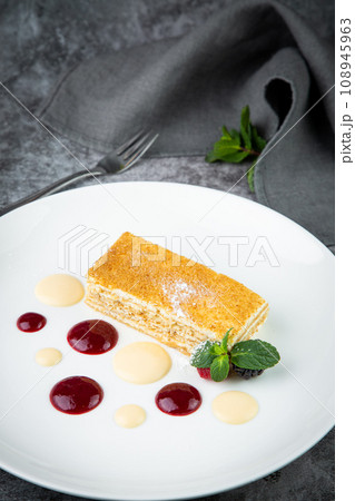 white sponge cake with drops of syrup, mint and wild berries on a round plate side veiw 108945963