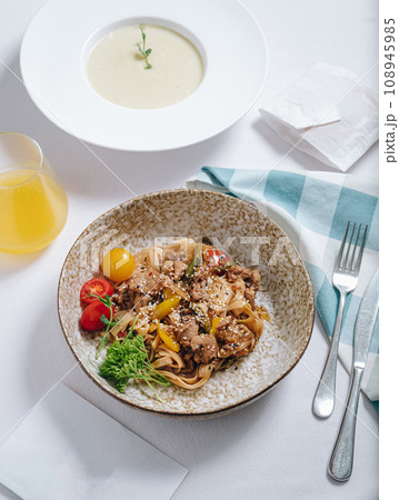 udon noodles with duck meat, herbs, sesame seeds and cherry tomatoes side view 108945985