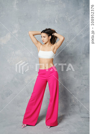 Young woman in wide cherry pink trousers and white tube top pulling hair Young woman in wide cherry pink trousers and white tube top pulling hair 108952376