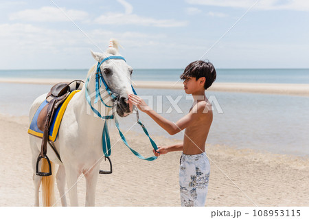 Young rider with horse standing on the beach. 108953115
