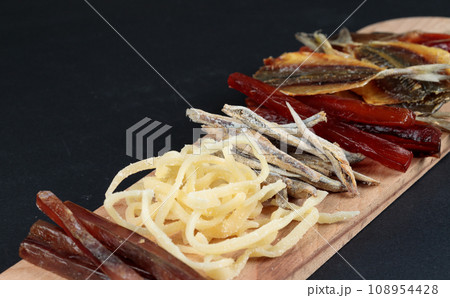 Salty snacks with beer and ale. Dried fish, squid, delicacies. Close-up on a black background. Salty snacks with beer and ale. Dried fish, squid, delicacies. Close-up on a black background. 108954428