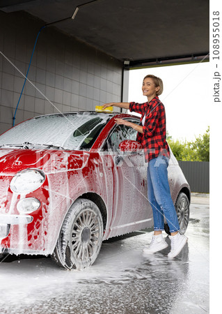 Woman in red checkered shirt washing the car and looking busy 108955018