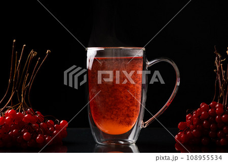 Hot viburnum tea in a glass cup with a double bottom on a black background. Hot viburnum tea in a glass cup with a double bottom on a black background. 108955534