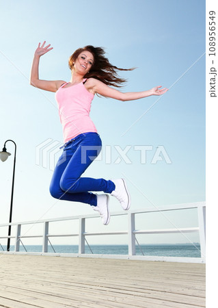 Attractive girl young woman jumping against blue sky Attractive girl young woman jumping against blue sky 108956549