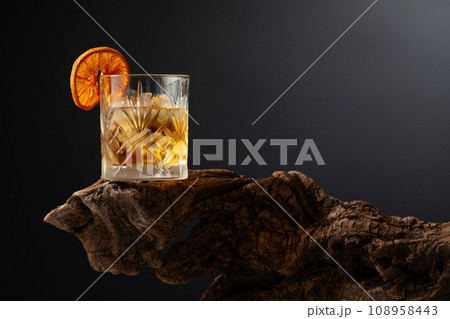 Old fashioned cocktail with ice and dried orange slice on a old snag. 108958443
