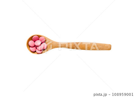 Vitamin capsules in a spoon on a colored background. Pills served as a healthy meal. Red soft gel vitamin supplement capsules on spoon 108959001