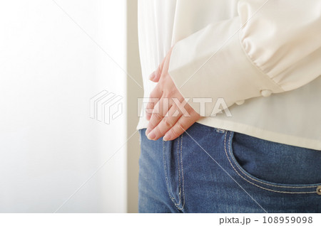 お腹が痛そうに手を当てている女性 108959098