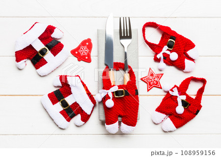 Festive set of fork and knife on wooden background. Top view of new year decorations and santa clothes and hat. Close up of christmas concept Festive set of fork and knife on wooden background. Top view of new year decorations and santa clothes and hat. Close up of christmas concept 108959156