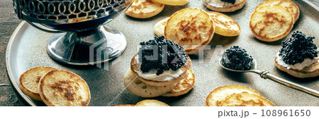 Blinis with black caviar panorama. Mini pancakes on a festive dish Blinis with black caviar panorama. Mini pancakes on a festive dish 108961650