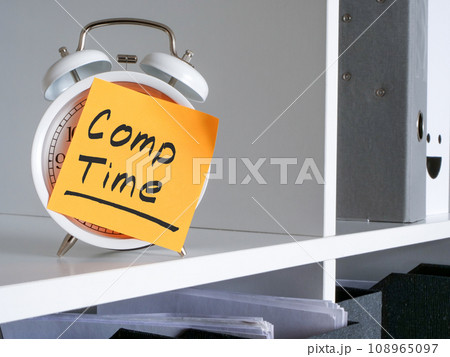Alarm clock on an office shelf and compensation Comp time inscription. Alarm clock on an office shelf and compensation Comp time inscription. 108965097