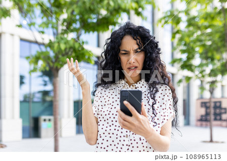 Sad disappointed woman received online notification with bad news on her phone, businesswoman walking outside office building, using application on smartphone, reading social media unsatisfied. 108965113