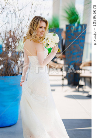 Beautiful blonde bride in a tight-fitting dress with a bouquet.  108966078