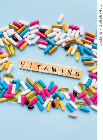 Health and medicine concept. Bright different types of medicines for health. Medicines on a blue background with a wooden inscription vitamins, vertical photo. 108967451
