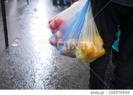 A man holds plastic bags in his hand with vegetables A man holds plastic bags in his hand with vegetables 108976699