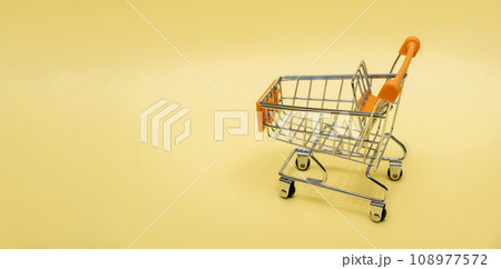 Small cart on a yellow background. Small supermarket grocery push cart for shopping. Shopaholic. Buyer. Shopping concept. Close-up. Isolated shopping trolley on a yellow background. Copy space. 108977572
