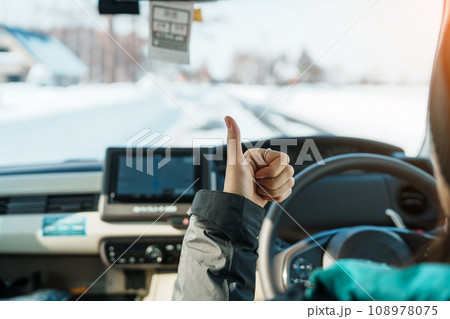 Happy Traveler driving car on snowy road and gesture finger up, woman Tourist enjoying snow forest view from the car in winter season. Winter travel, Road trip, Exploring and Vacation concepts 108978075