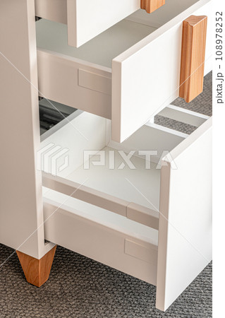 Stylish white office commode with wooden handles and legs with open empty drawers closeup view. Comfortable furniture for home and office furnishing Stylish white office commode with wooden handles and legs with open empty drawers closeup view. Comfortable furniture for home and office furnishing 108978252