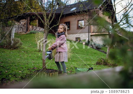 Little girl watering tree in garden, using collected rainwater. Concept of water conservation in garden and family gardening. 108978625